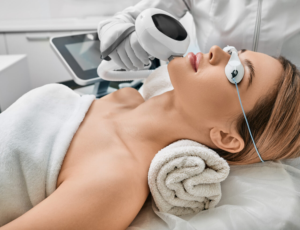 Photorejuvenation, rosacea treatment, removing brown spots and vascular mesh. Cosmetologist using IPL apparatus treats skin of female patient's face