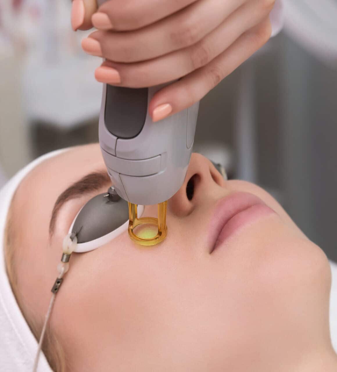 Therapist beautician makes a laser treatment to young woman's face at beauty SPA clinic. Facial laser hair removal epilation procedures. Face care rejuvenation medical correction for model by apparatus in salon. Close up, selective focus.